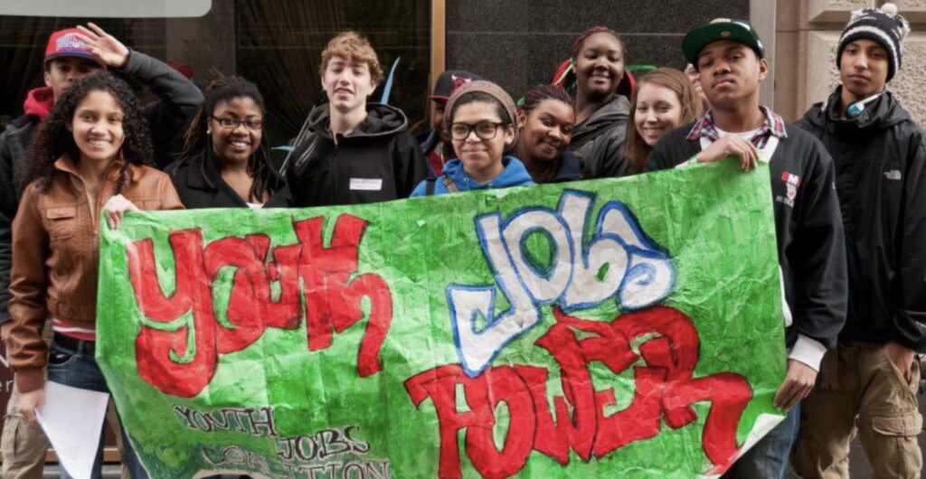 Youth participants of Dudley Street Neighborhood Initiative holding a banner that reads "youth power, jobs"